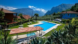 A swimming pool with a view of mountains, surrounded by greenery and a small gazebo. - Residence Christina Due Laghi (Tenno)