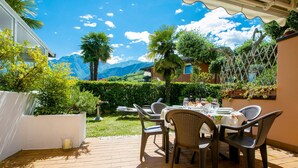 An outdoor patio with a table set for dining, surrounded by chairs, and a view of mountains in the background. - Residence Christina Due Laghi (Tenno)