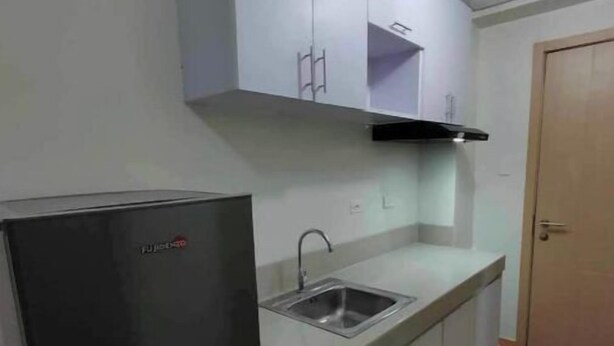 Eine kleine Küche mit einem schwarzen Kühlschrank, einer Spüle und hellen Schränken.