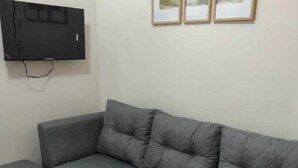 Ein graues Ecksofa mit passendem Hocker, ein Flachbildfernseher an der Wand und drei gerahmte Bilder über dem Sofa.