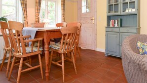 A dining area with a wooden table and chairs, a wicker armchair, and a blue cabinet with glass doors. - Doppelhaus in Oldsum auf Foehr (Oldsum)