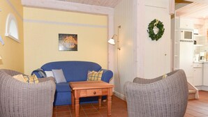 A cozy living room with a blue sofa, two wicker chairs, a wooden coffee table, and a painting on the wall. - Doppelhaus in Oldsum auf Foehr (Oldsum)