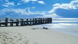 A wooden pier extending into a beach with clear skies and calm waters. - Doppelhaus in Oldsum auf Foehr (Oldsum)