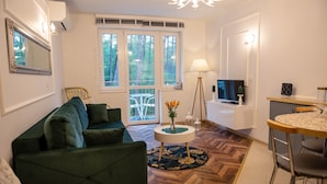 A modern living room with a green sofa, a round coffee table with a floral rug, a TV, and a dining area with a small table and chairs. - Apartment in Pobierowo Near Baltic Beach (Rewal)