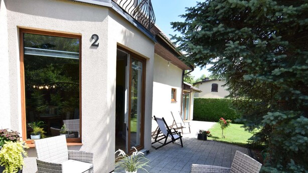 Une maison moderne dotée d’un patio aménagé avec des meubles en osier et une table en verre.
