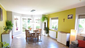 Un salon lumineux comprenant un coin repas, un canapé gris, une table basse et une vue sur le jardin grâce à de grandes fenêtres.
