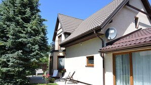 Une maison à deux étages, dotée d’un toit en pente, d’une antenne parabolique et d’une grande fenêtre avec des rideaux.