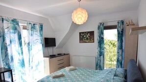 Une chambre à coucher avec un lit, un bureau, une télévision et une fenêtre avec des rideaux.