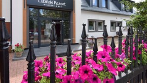Das Lubinski Resort, ein Hotel mit Schwerpunkt auf Wellness und Spa, zeichnet sich durch eine moderne Fassade und einen schmiedeeisernen Zaun mit leuchtenden Blumen aus.