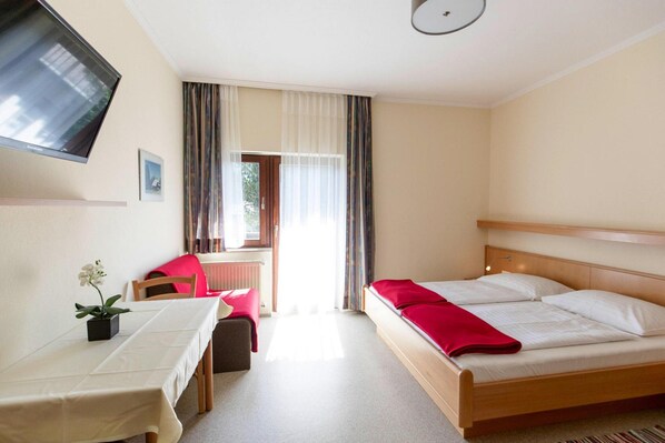 Ein Hotelzimmer mit Bett, Schreibtisch, Stuhl, Fernseher und einem Fenster mit Vorhängen.