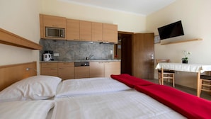 Ein Hotelzimmer mit einem Bett, einer roten Decke, einer Küchenzeile inklusive Mikrowelle, einer Kaffeemaschine und einem an der Wand befestigten Fernseher.