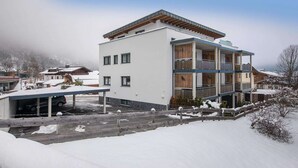 A modern multi-story building with a covered parking area and a balcony.