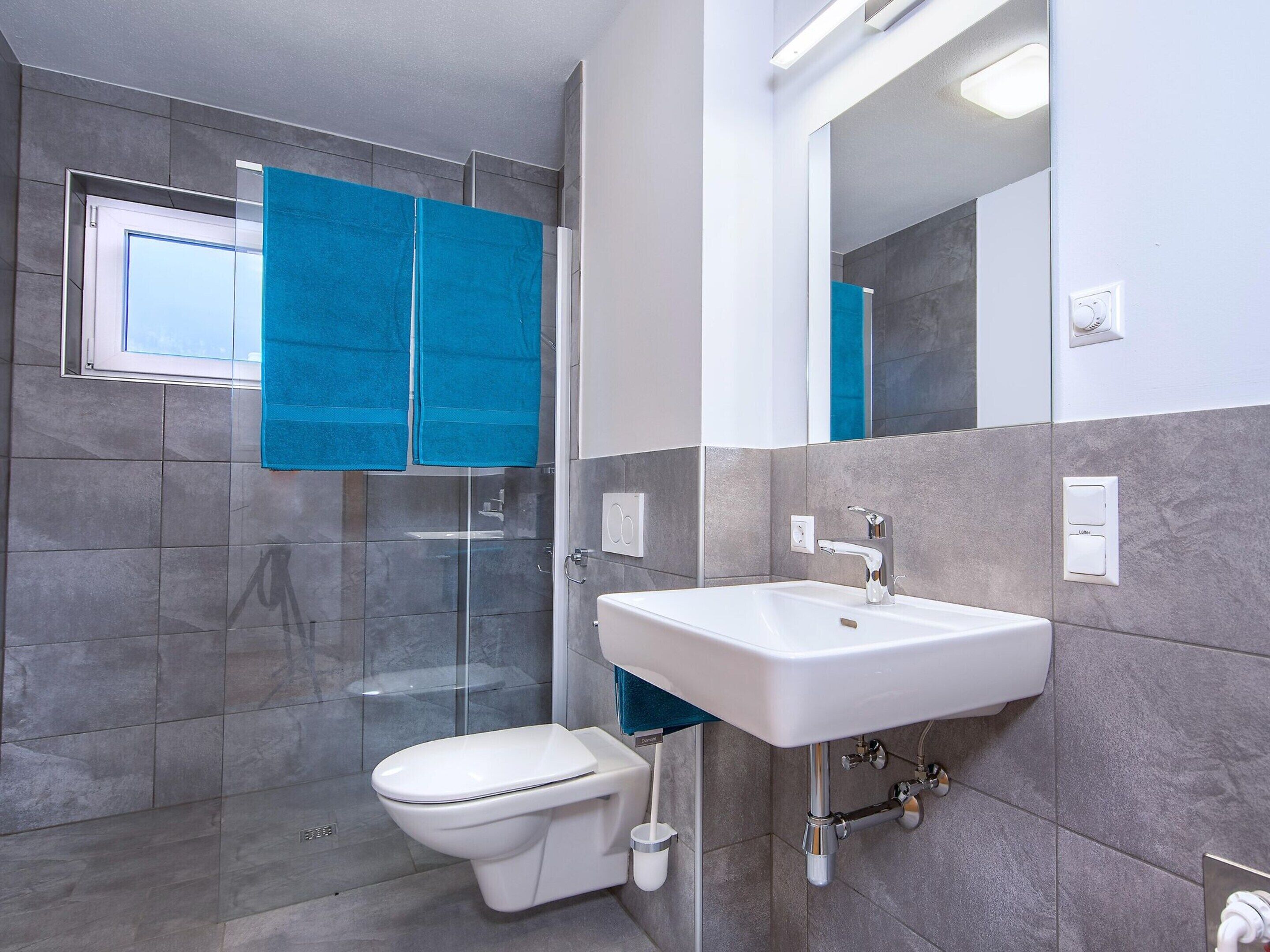 Une salle de bain moderne avec une douche à parois de verre, des toilettes blanches et un lavabo avec des robinetteries chromées.