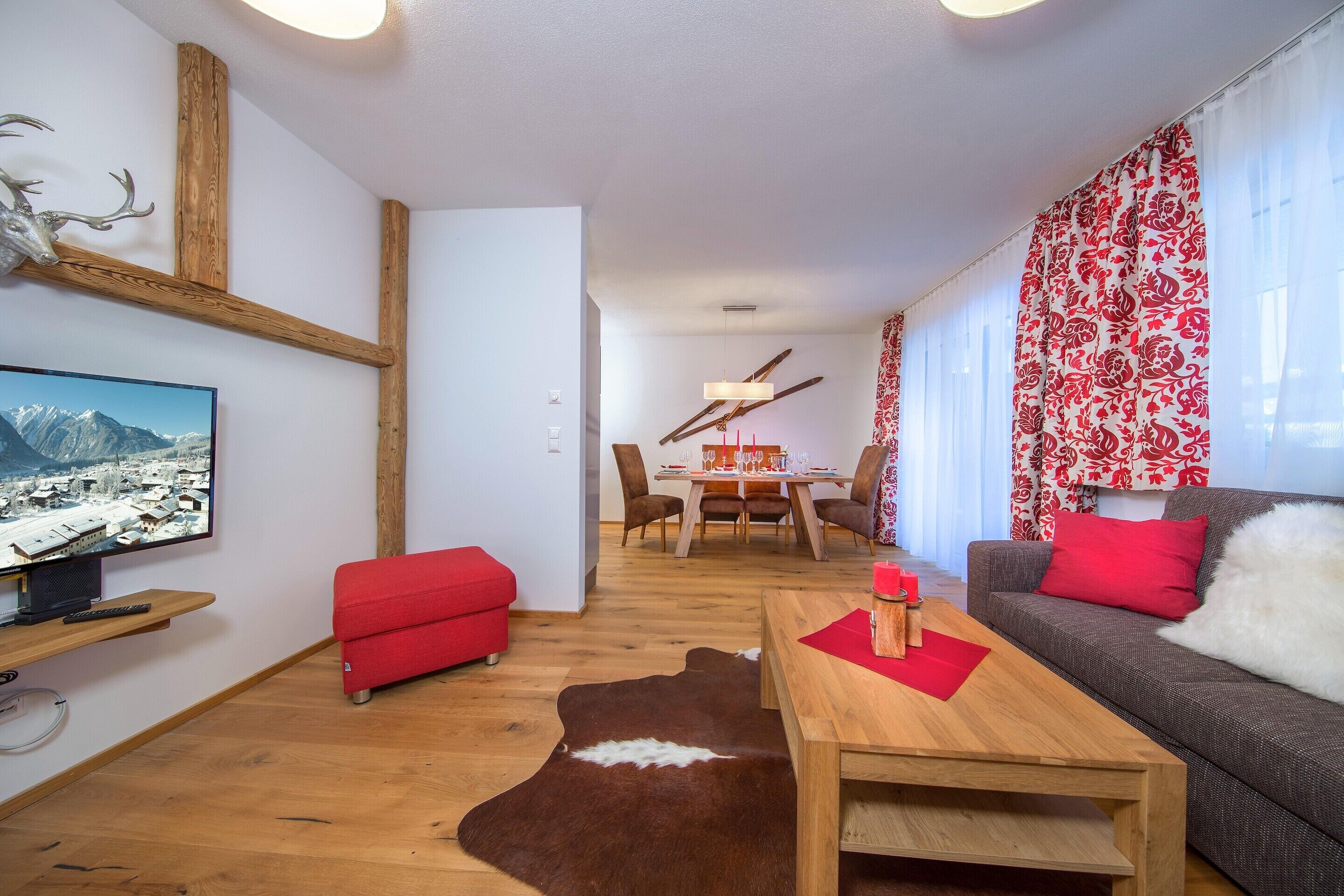 A modern living room with a wooden floor, a red sofa, a brown leather rug, and a dining area with a table and chairs.