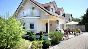 Ein zweistöckiges Haus mit Balkon, einer Terrasse und Gartenmöbeln sowie gepflegter Bepflanzung.