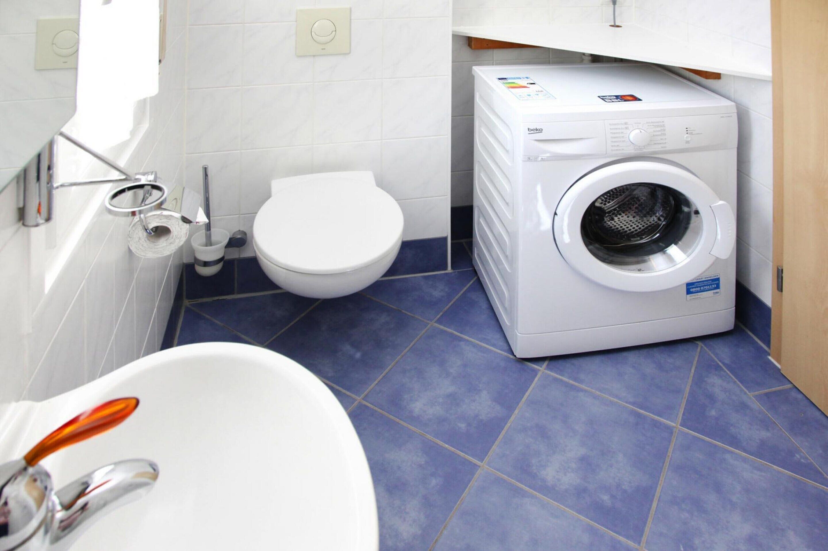 A bathroom with a white toilet, a washing machine, and a bathtub.