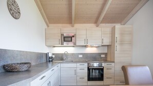 A modern kitchen with wooden cabinets, a built-in microwave, a stove, and a coffee maker. - Gemutliches, Exklusives Ferienhaus in Dagebull (Dagebuell)