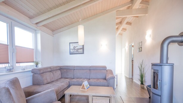 A modern living room with a sectional sofa, a wooden coffee table, and a wood-burning stove. - Gemutliches, Exklusives Ferienhaus in Dagebull (Dagebuell)