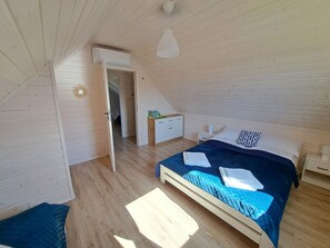 A bedroom with a wooden ceiling, a bed with a blue quilt, a bedside table, and a nightstand. - Holiday Home in Niechorze Near Lighthouse (Rewal)