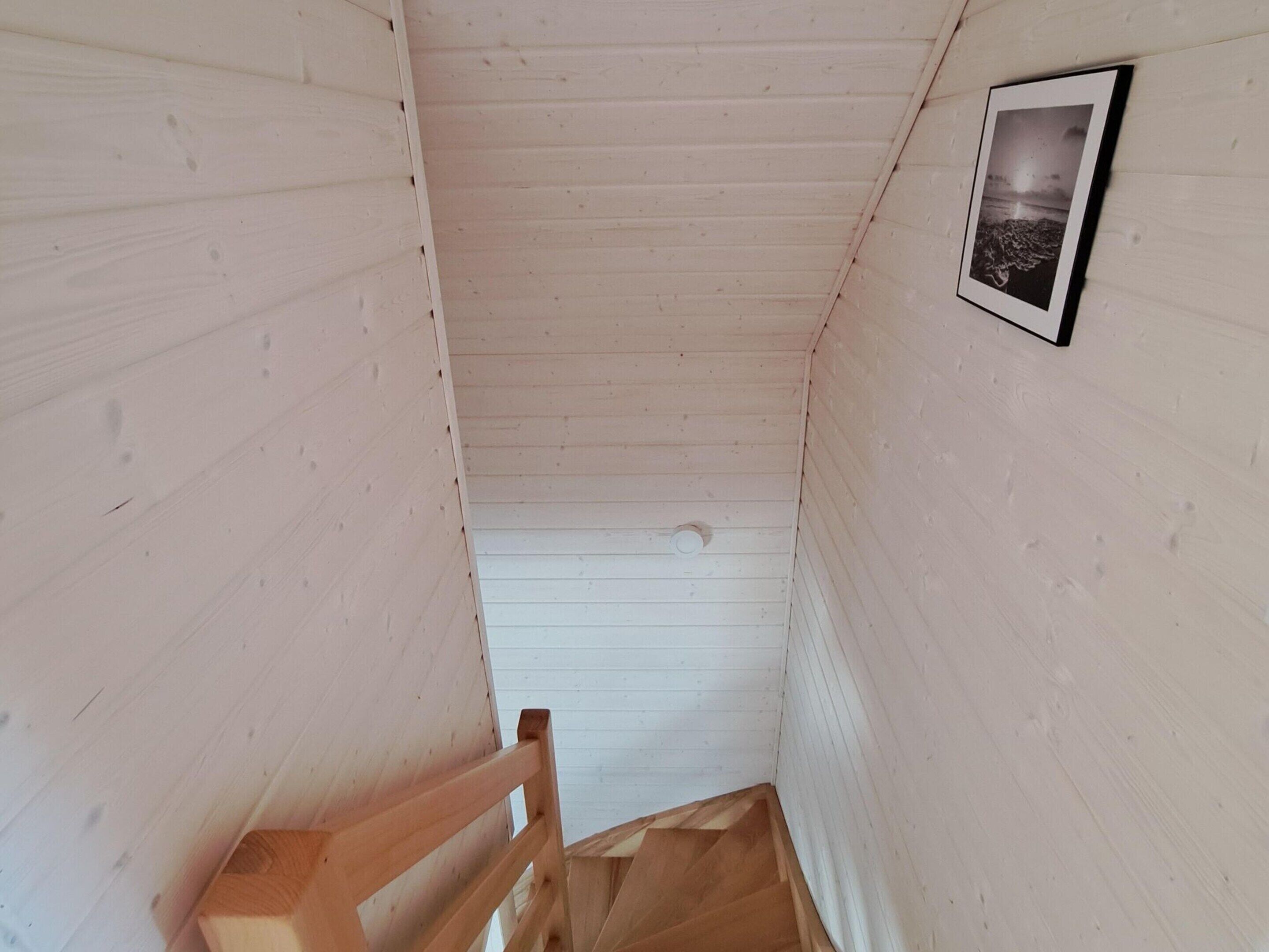 A narrow wooden staircase leading to a landing with a framed picture on the wall.
