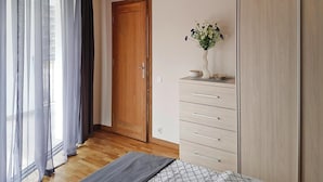 Egy hálószoba, melyben van egy fa ajtó, egy fiókos komód, egy éjjeliszekrény, melyen egy virágos váz áll, és egy mennyezetről lógó lámpatest.