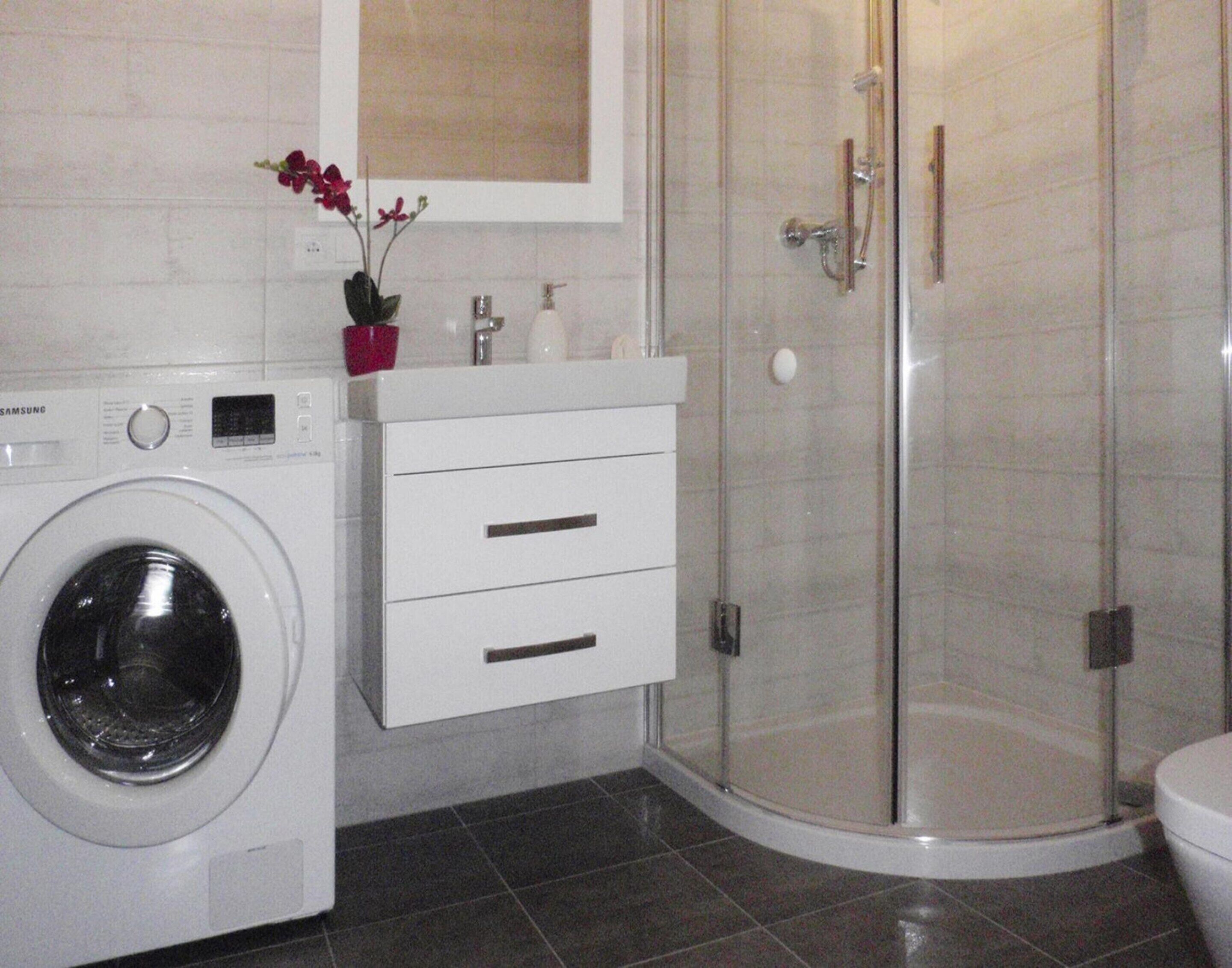Ein kleines Badezimmer mit Waschmaschine, Duschkabine und Toilette.