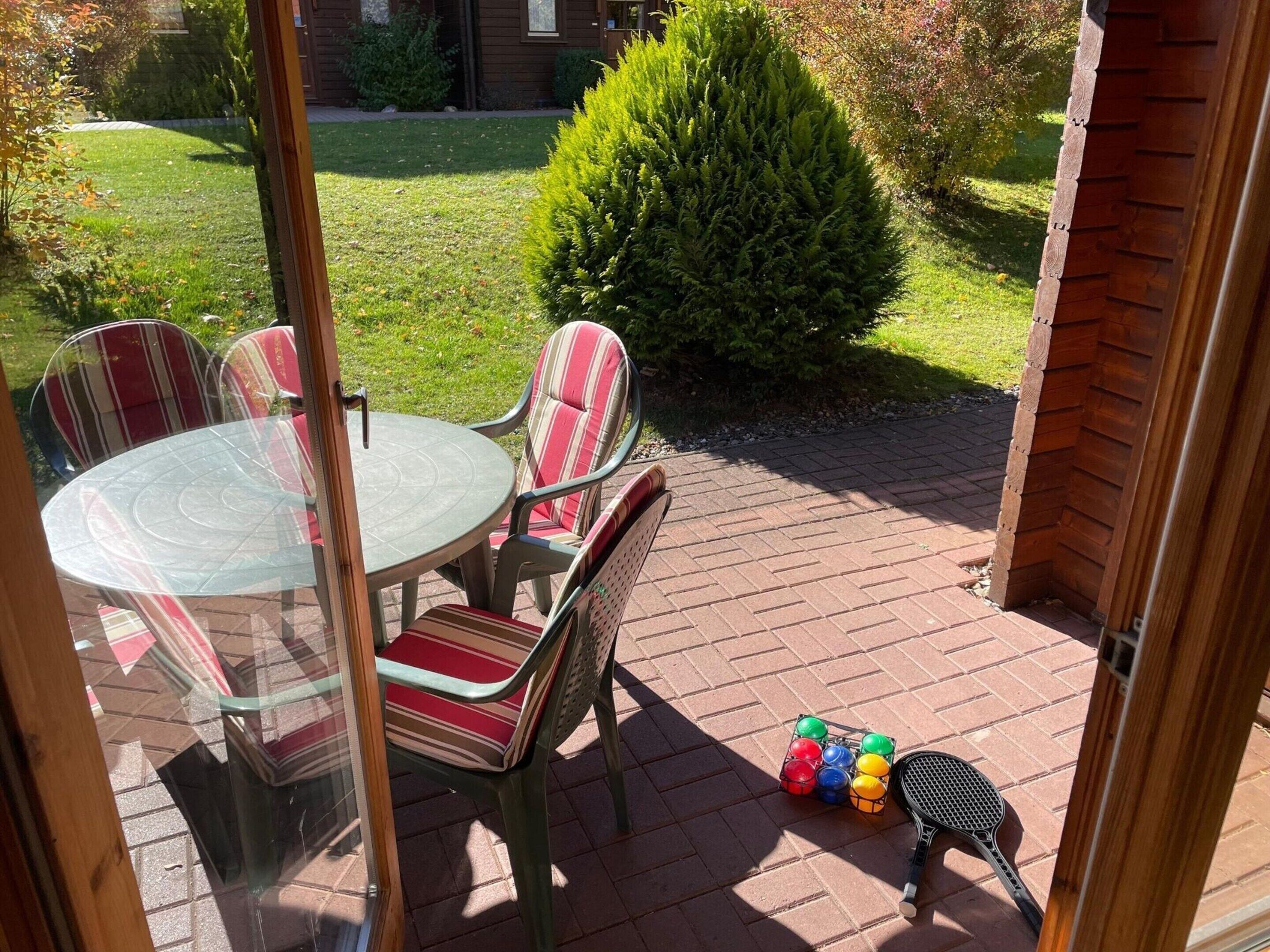 A patio with a round glass table and striped chairs, a tennis racket, and colorful balls.
