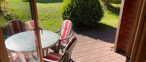 A patio with a round glass table and striped chairs, a tennis racket, and colorful balls.