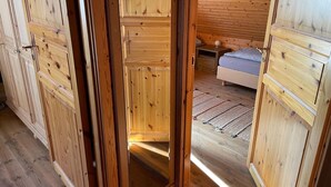 Un interior de madera con una puerta corredera que da a un dormitorio con cama y mesita de noche.