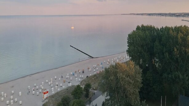 A beach with rows of white tents and a pier extending into the water. - Ferienwohnung in der Mecklenburger Seenplatte (Buchholz)