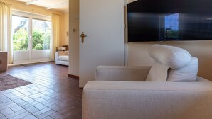 A hotel room with a large window, a flat-screen TV mounted on the wall, a sofa, and a door leading to a balcony. - Thatched Roof House in St.peter Ording (St. Peter-Ording)