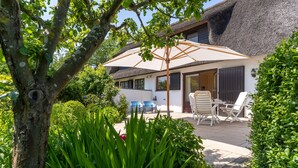 A house with a thatched roof, a patio with outdoor furniture, and a garden with various plants. - Thatched Roof House in St.peter Ording (St. Peter-Ording)