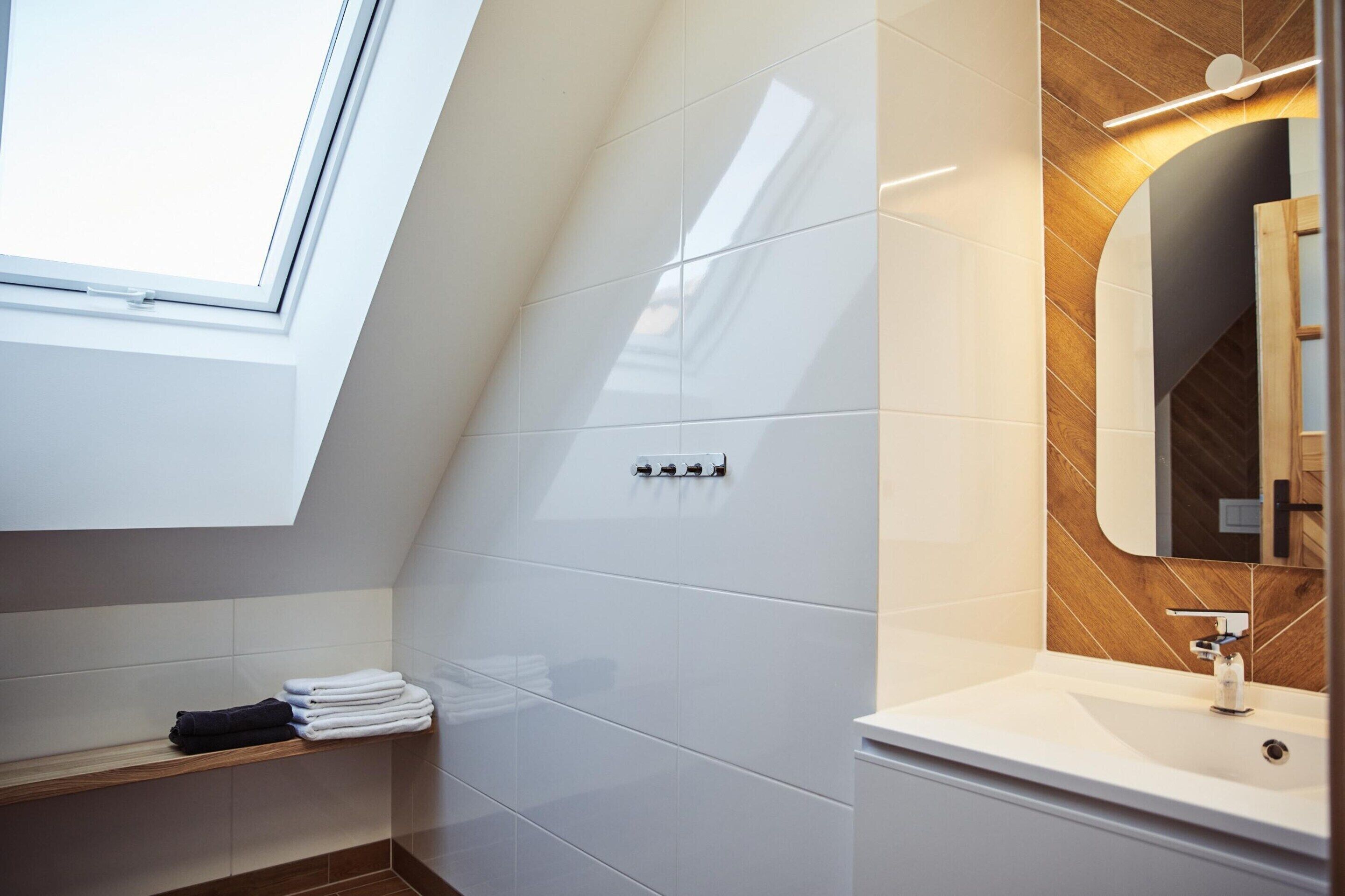 A modern bathroom with a skylight, white tiles, a wooden vanity, and a mirror.