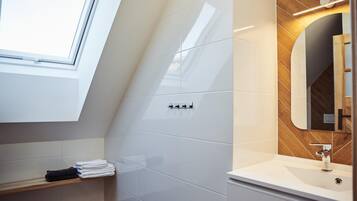A modern bathroom with a skylight, white tiles, a wooden vanity, and a mirror.