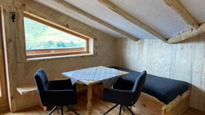 A small, cozy room with a wooden interior, a table with two chairs, a bed, and a window with a view of greenery. - Chalet in Zillertal Near Hochzillertal Ski Area (Zellberg)
