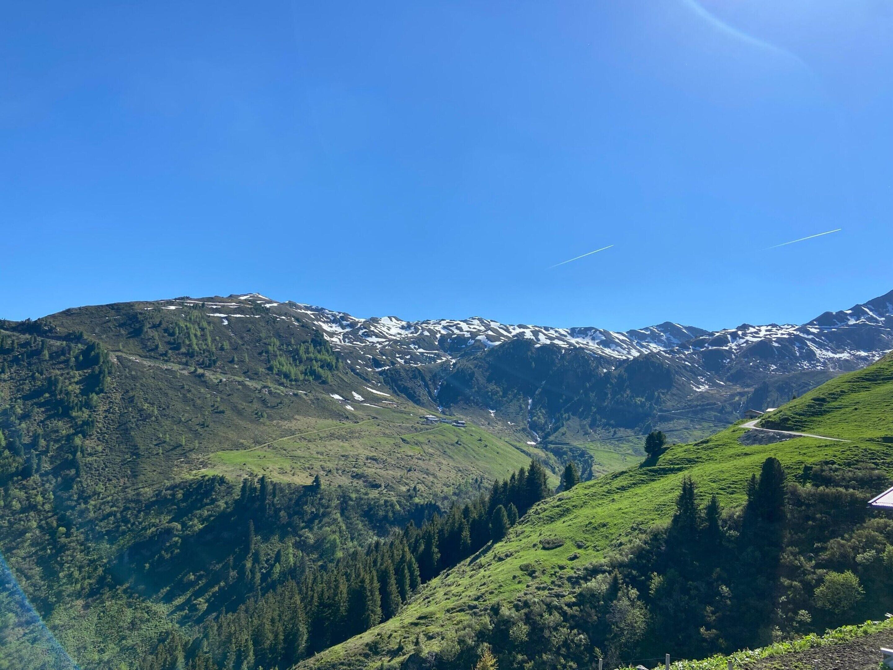 A mountainous landscape with snow-capped peaks, a valley with greenery, and a clear sky.