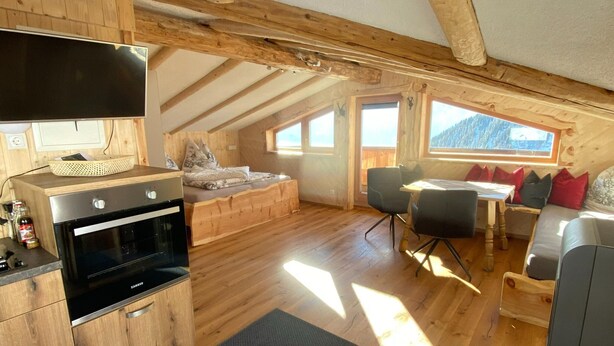 A cozy attic bedroom with a bed, a small kitchenette, and a dining area with a table and chairs. - Chalet in Zillertal Near Hochzillertal Ski Area (Zellberg)