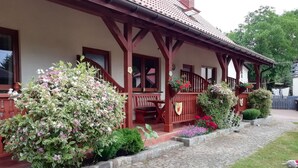 A traditional wooden house with a porch, stone pathway, and various plants. - Kolczewo Cottage With BBQ & Garden (gmina Wolin)