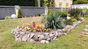 A garden with a variety of plants and flowers, a stone border, and a wooden fence in the background. - Kolczewo Cottage With BBQ & Garden (gmina Wolin)