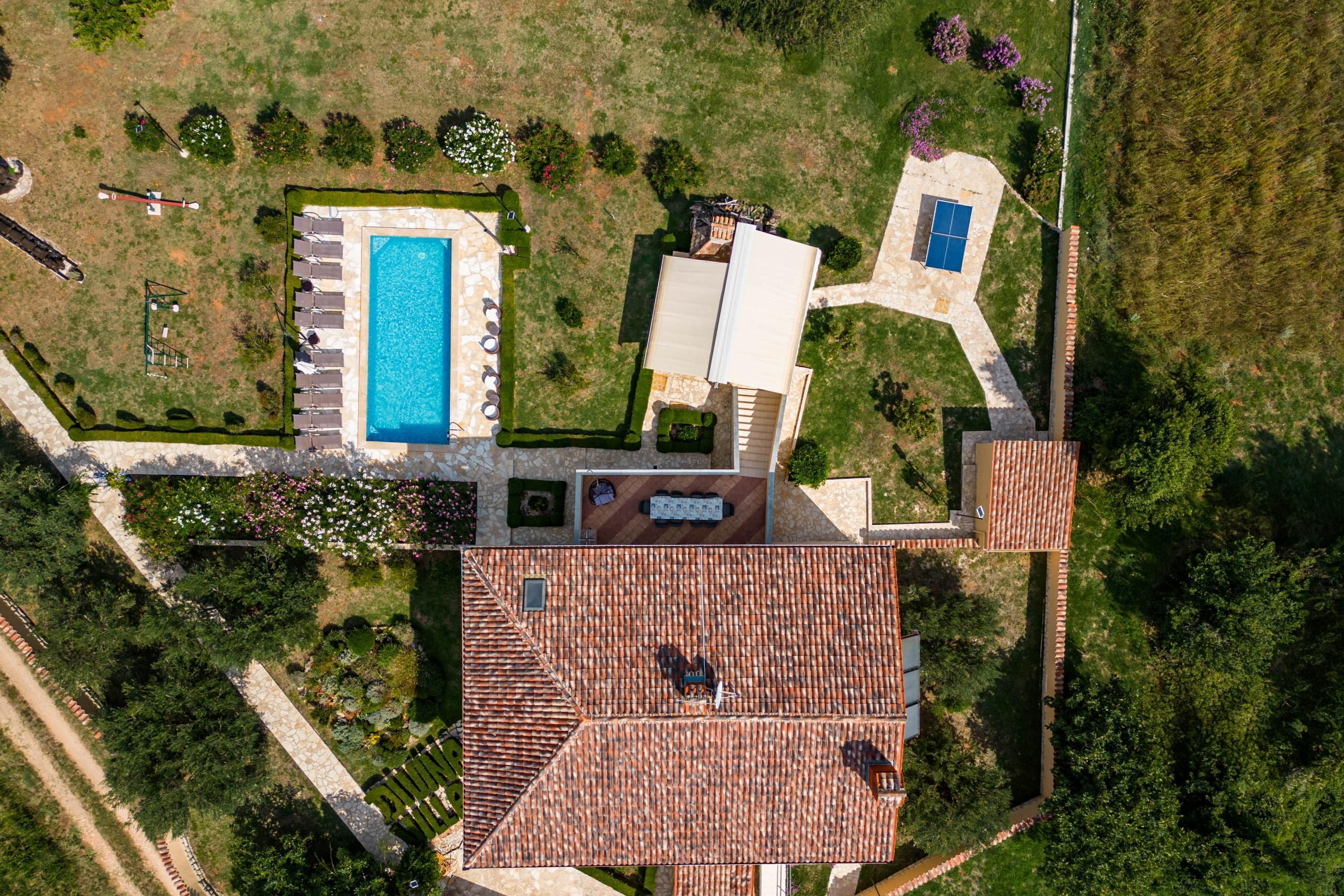 An aerial view of a property with a swimming pool, a tennis court, and a covered patio area.