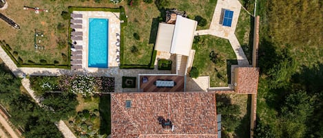 An aerial view of a property with a swimming pool, a tennis court, and a covered patio area.
