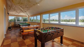 Una habitación con mesa de futbolín, mesa de billar y ventanas amplias con vistas a zonas verdes.