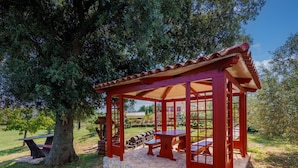 Un mirador de madera roja con base de piedra, rodeado de árboles y un área de picnic.