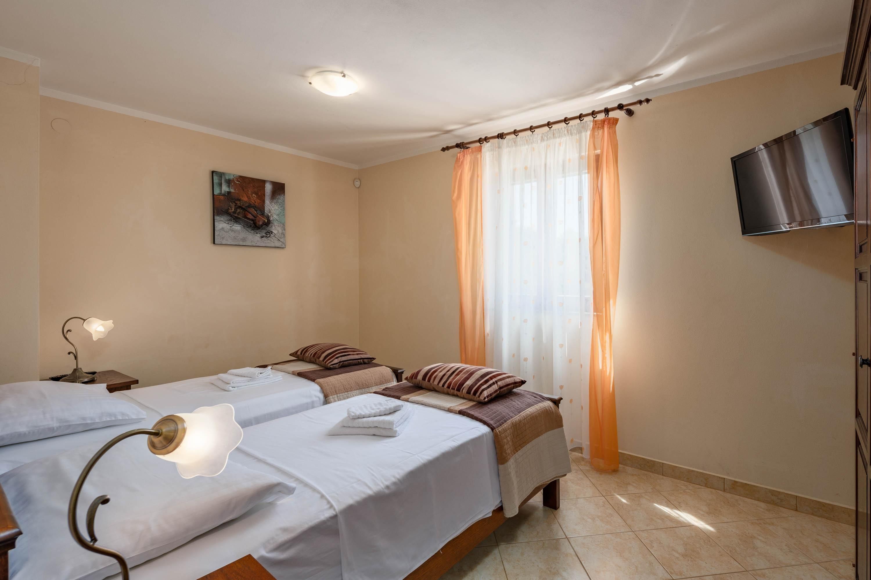 A hotel room with two beds, a flat-screen TV, a painting on the wall, and a window with curtains.