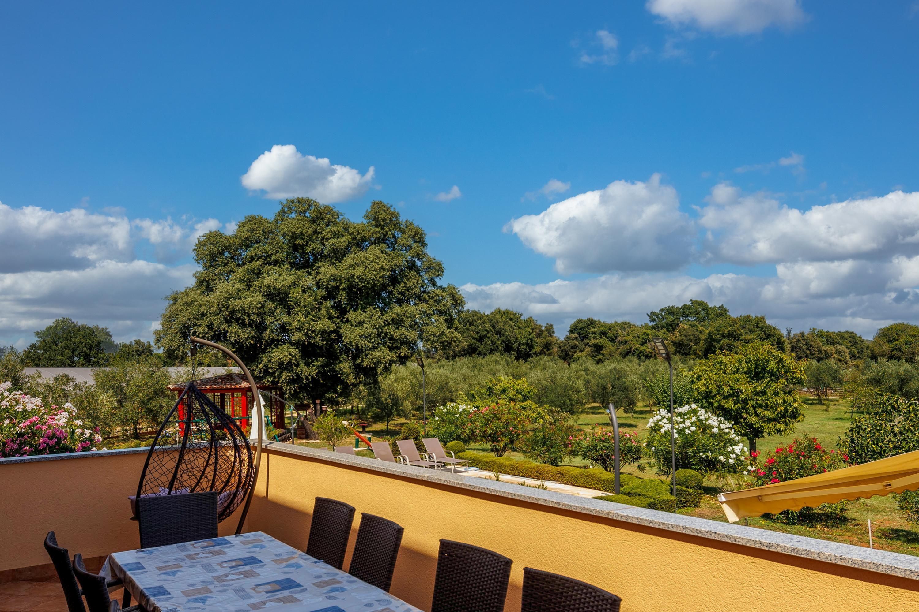 Une terrasse avec une table et des chaises, donnant sur un jardin agrémenté d’arbres et de fleurs.