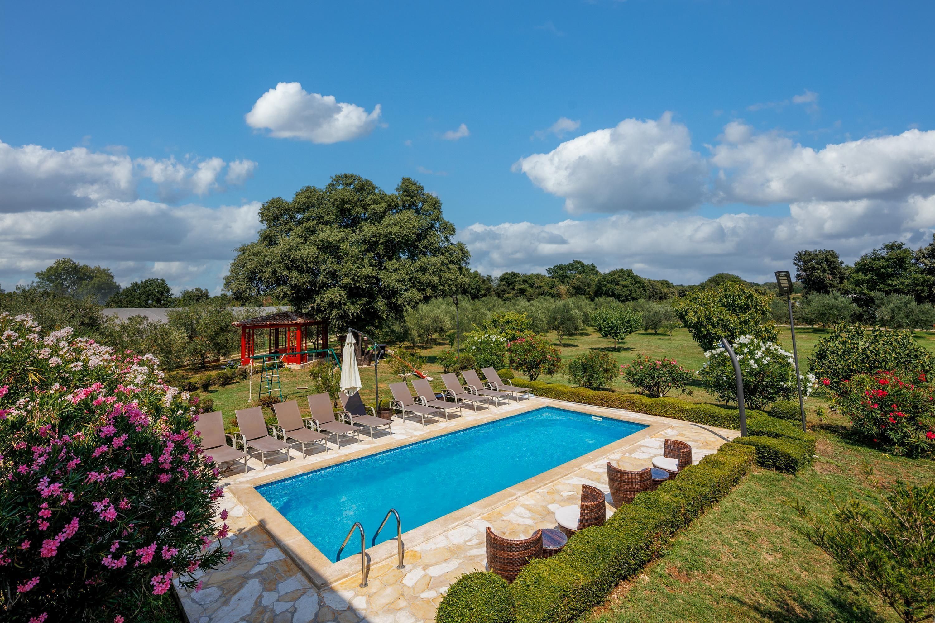 A rectangular pool with lounge chairs and a gazebo in a landscaped garden.