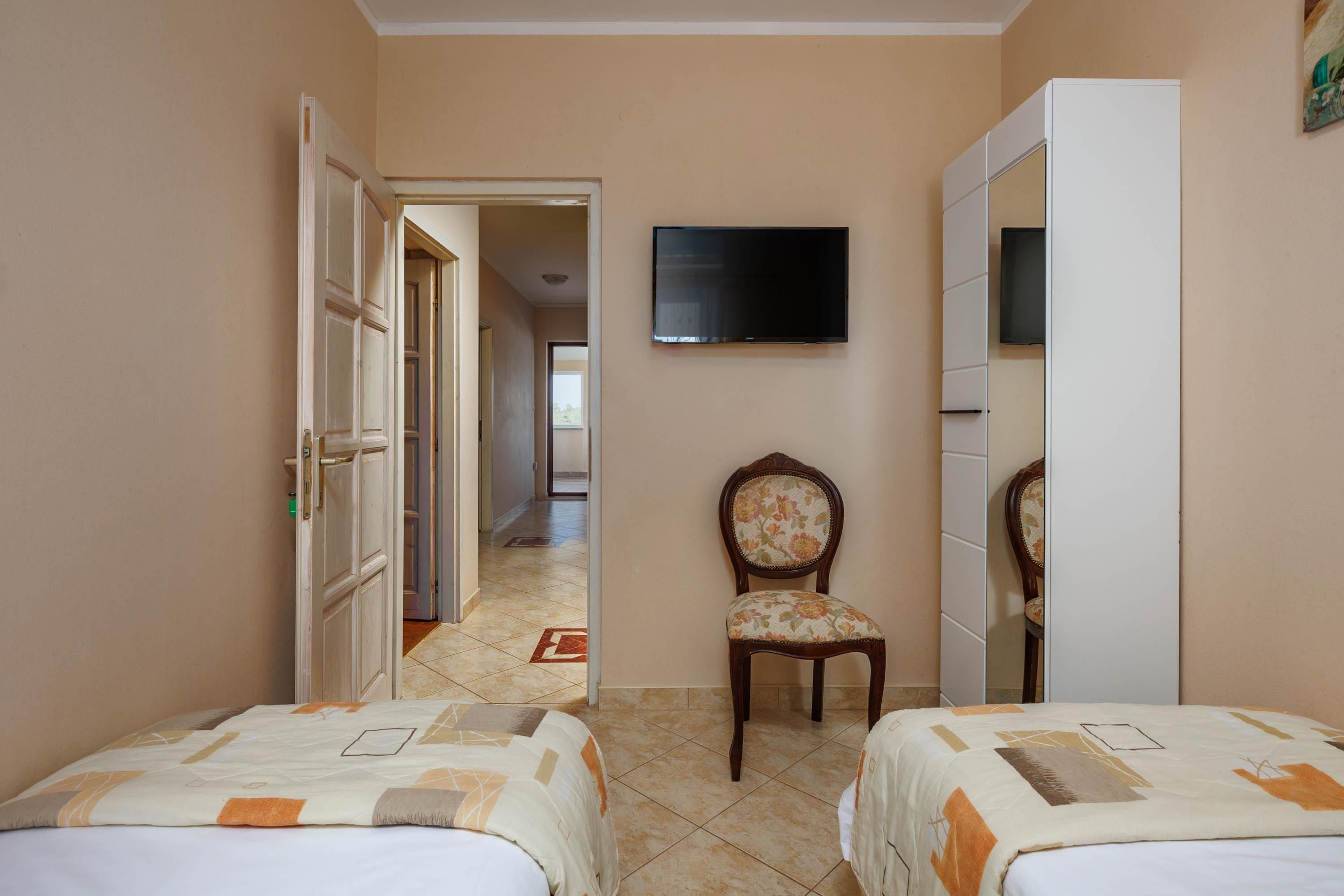 Habitación de hotel con dos camas, televisor, una silla y armario.