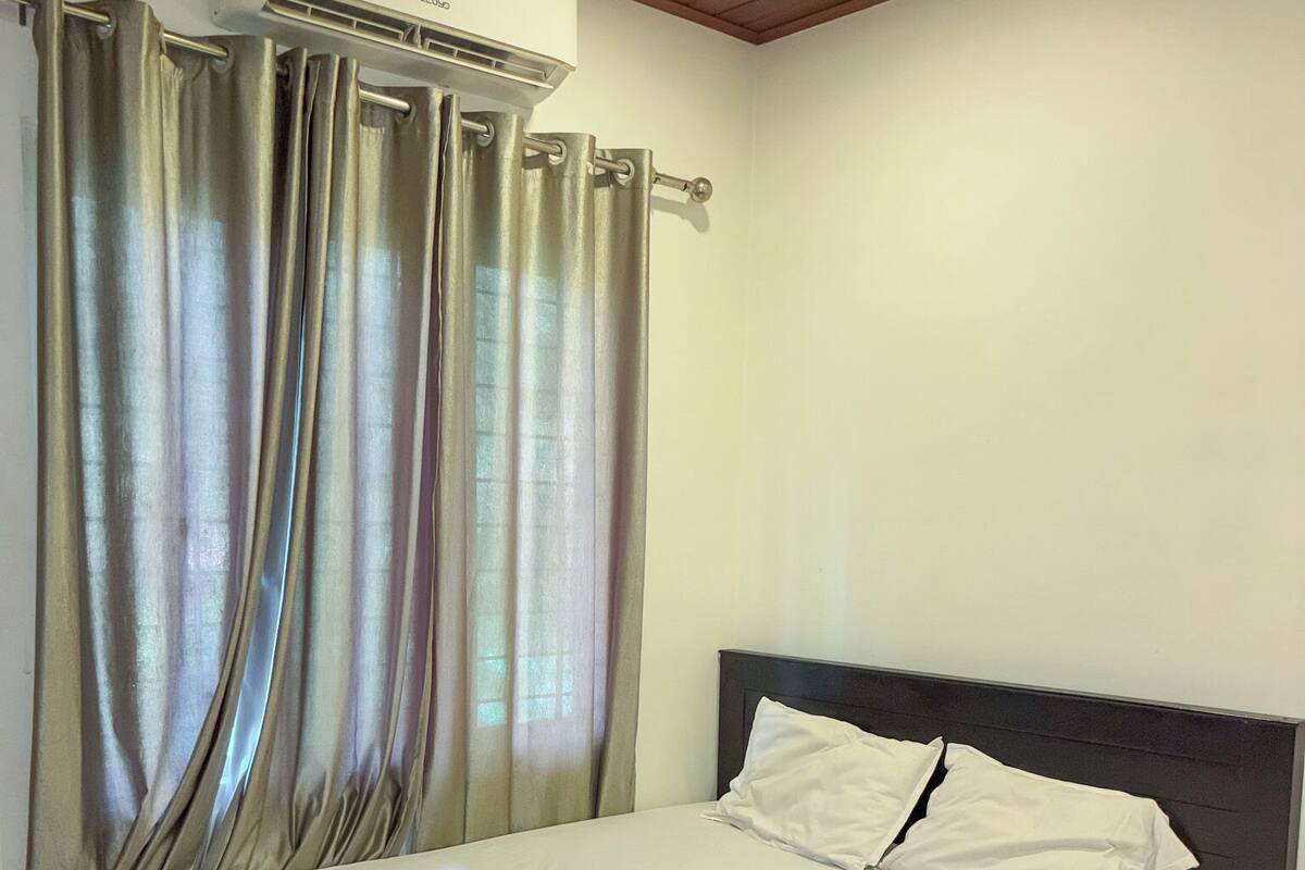 A neatly made bed with a brown bedspread, a headboard, and a wall-mounted air conditioner.