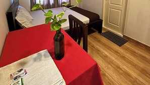 Una habitación con una mesa roja, una silla, una planta, una cama, una ventana con cortinas, un equipo de aire acondicionado y una puerta.