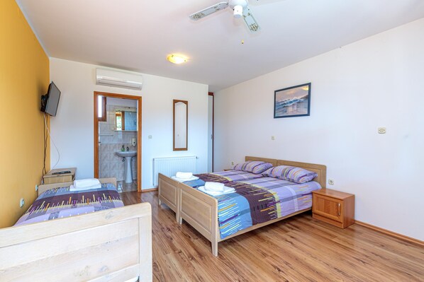 A bedroom with a wooden bed, a bedside table, a nightstand, a ceiling fan, a wall-mounted TV, and a bathroom visible through an open door. - Pool Fun House Betiga 1 With gym (Vodnjan)
